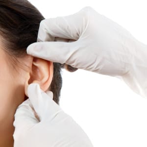 Gloved hands assessing a woman's ear