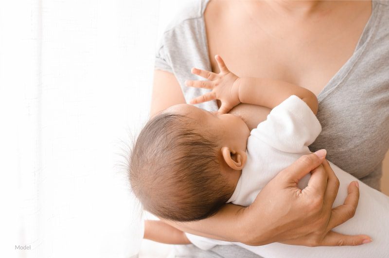 Mother nursing her baby, which can be impacted by breast enhancement surgery.