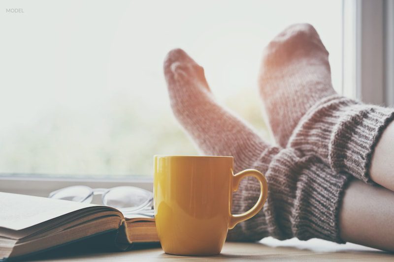 Close up image of woman's feet while she is resting next to a cup of tea.