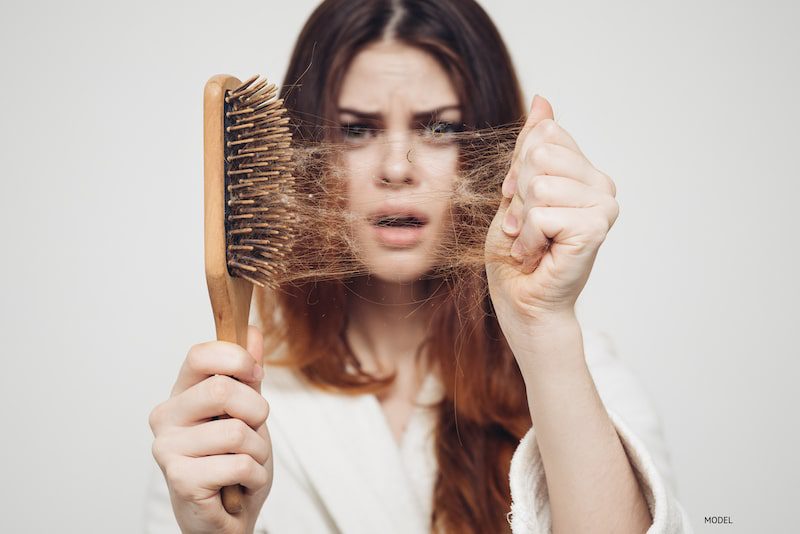 Woman pulling hair from her hairbrush to show hair loss