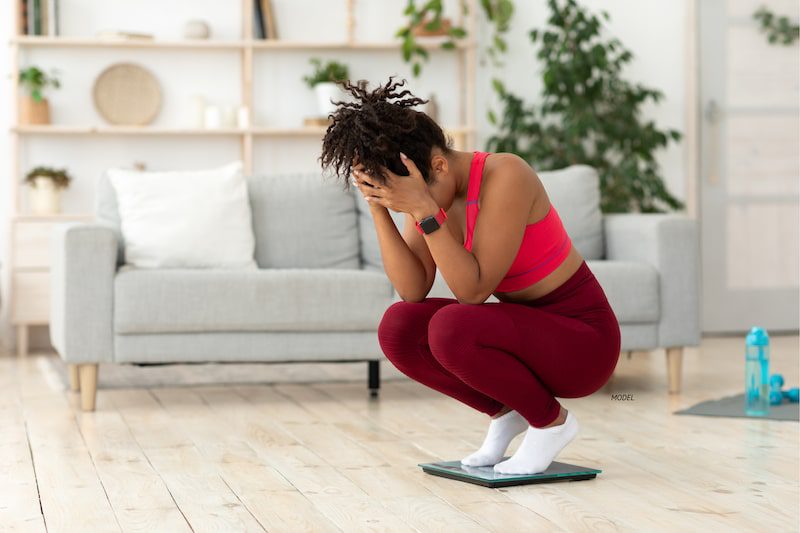 Frustrated women crouching on a scale.