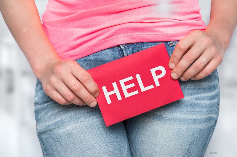 Woman holding a sign that says help over the upper part of her pants.