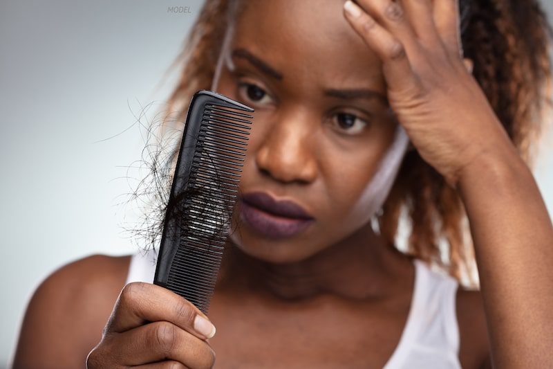 Frustrated woman looking at her lost hair in a comb.