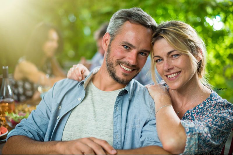 Attractive middle-aged couple smiling at the camera while leaning into each other affectionately