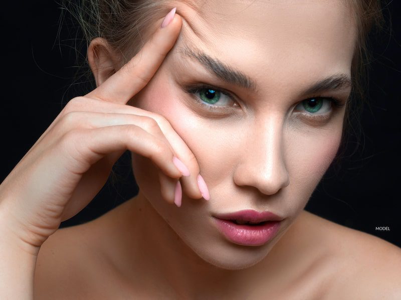 Woman lifting her brow with her finger. 