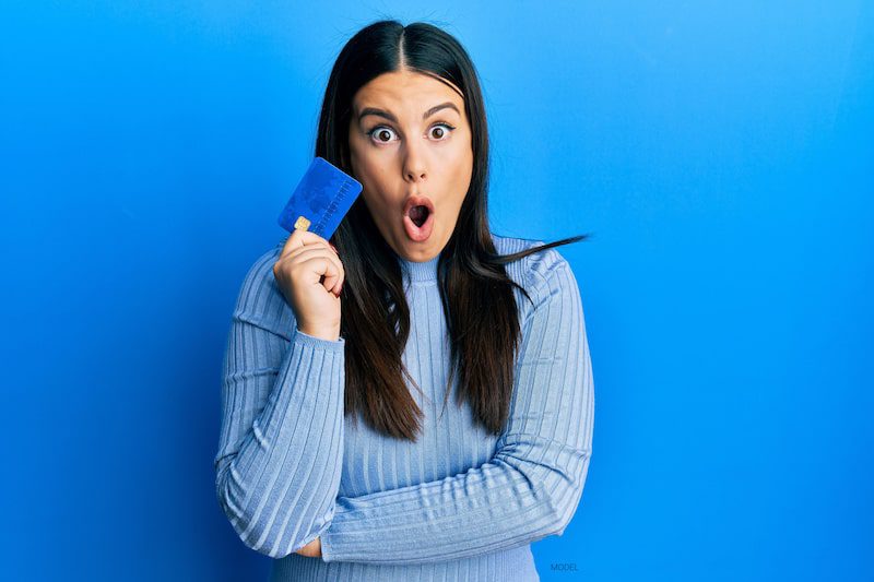 A woman with a surprised expression holds up a credit card.